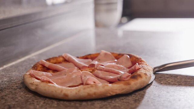 Tracking shot pizza being transferred from prep counter into hot oven in pizzeria kitchen.