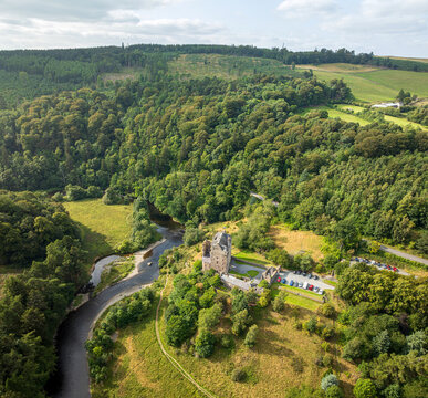 Aerial view of Neidpath Castle situated along the River Tweed, surrounded by dense woodland and rolling green hills in Peebles, Scotland, United Kingdom.