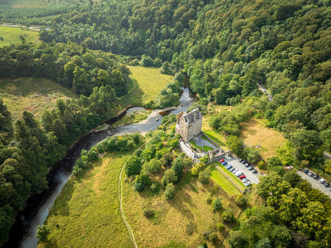 Aerial view of Neidpath Castle situated by the River Tweed surrounded by lush green forests and grassy fields in Peebles, Scotland, United Kingdom.