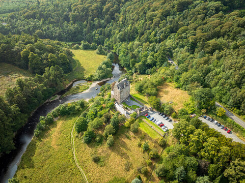 Aerial view of Neidpath Castle situated on the banks of the River Tweed, surrounded by lush green forests and rolling hills in Peebles, Scotland, United Kingdom.