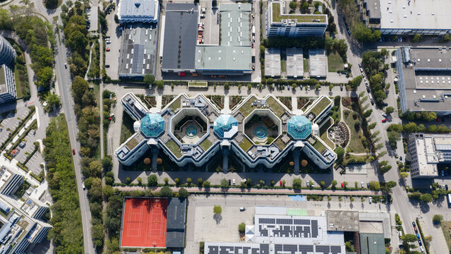 Aerial view of the NEXT building complex featuring a distinctive X-shaped design with glass domes and green roofs, surrounded by parking and industrial areas in Aschheim, Bayern, Germany.