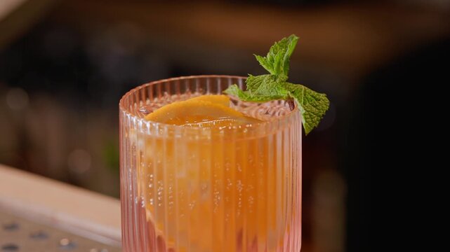 Slow motion mint garnish being placed onto citrus cocktail on bar counter.