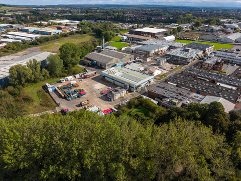 Aerial view of The Common featuring industrial warehouses, storage yards, and surrounding woodland in Stafford, England, United Kingdom.
