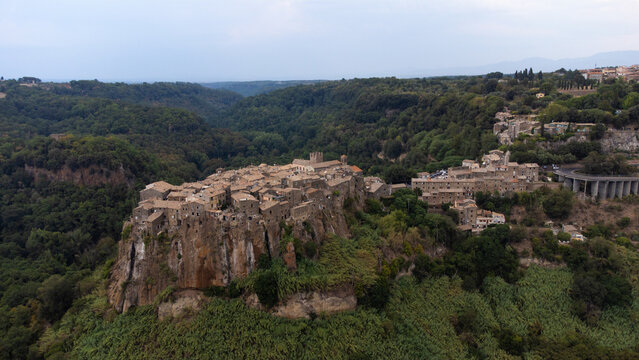 Aerial view of the historic hilltop village of Calcata Vecchia perched on a dramatic volcanic cliff surrounded by lush green forests in Calcata Vecchia, Lazio, Italy.
