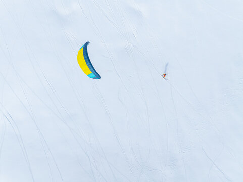 Aerial view of a snowkiter gliding across the vast, snow-covered terrain of the Trollstigen area with visible ski tracks in the snow, Fjord, More og Romsdal, Norway.