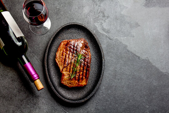 Grilled beef steak served on cast iron plate with red wine, tomato salad and potatoes ball.  Barbecue, bbq meat beef tenderloin. Top view, gray background