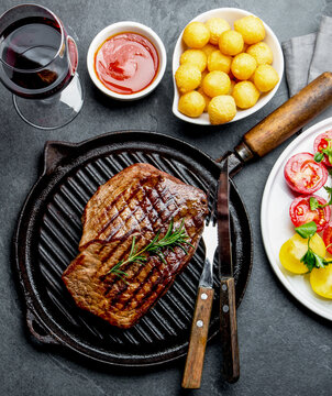 Grilled beef steak on grill pan served with tomato salad, potatoes balls and wine. Barbecue, bbq meat beef tenderloin. Top view, slate background