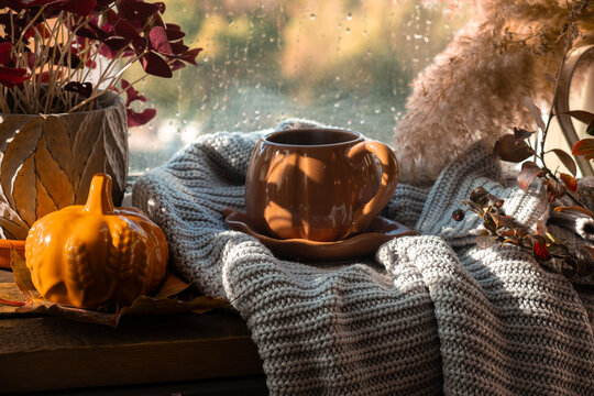 Autumn vibes. Cup of coffee or tea on windowsill in cozy interior, raining outside. Warm cozy fall mood. 