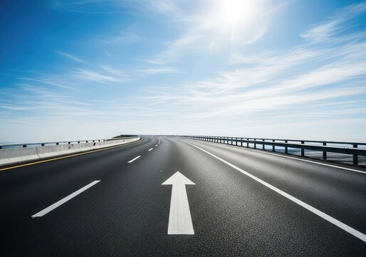 A winding paved highway stretches toward a bright horizon under a blue sky, featuring a prominent painted white arrow pointing forward, perspective, navigation, progress