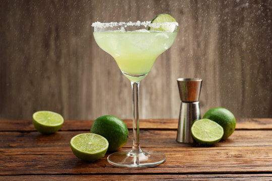 Refreshing margarita cocktail in glass, limes and jigger on wooden table, closeup