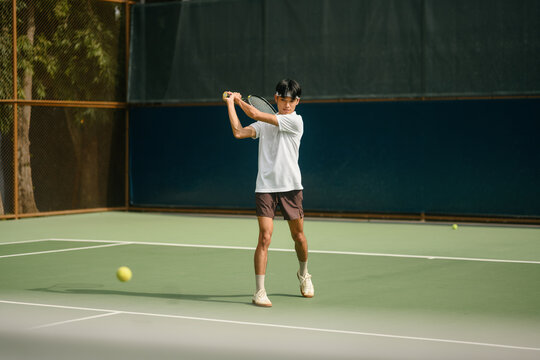 Young Asian Man Playing Tennis on Outdoor Court, Backhand Swing in Action