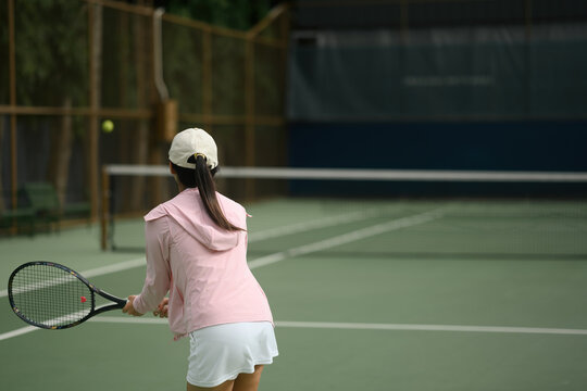 Rear view of Young Asian Woman Playing Tennis on Outdoor Court, Rear View with Racket Ready to Hit Ball