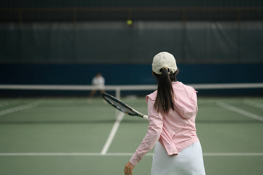 Rear view of Young Asian Woman Playing Tennis on Indoor Court, Rear View with Racket Following Through
