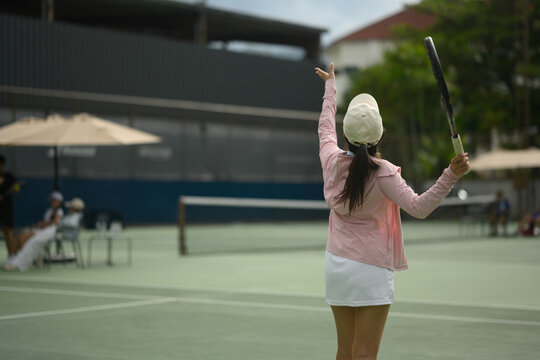 Rear view of Young Asian Woman Celebrating Victory on Outdoor Tennis Court with Racket Raised