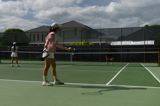 Wide angle of Young Asian Woman Preparing to Serve on Outdoor Tennis Court with Doubles Partners