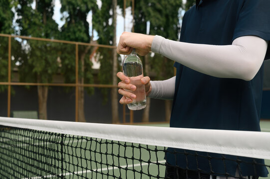Cropped of Tennis Player Opening Water Bottle at Net During Break on Outdoor Court