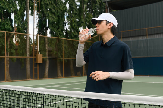 Asian Male Tennis Player Drinking Water at Outdoor Tennis Court Net