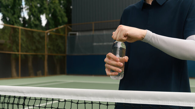 Close up of a Tennis Player Opening Water Bottle at Net During Match Break for Hydration and Recovery