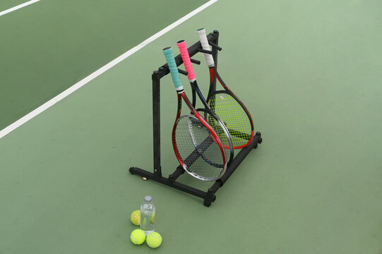 Tennis Rackets on Stand with Balls and Water Bottle on Green Court