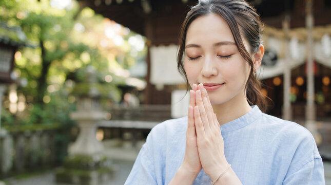 神社で目を閉じて手を合わせ静かに参拝する若い女性