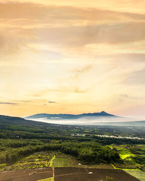 Aerial view of the mountainous landscape of Bumiaji with agricultural fields and lush greenery under a golden hour sky in Bumiaji, East Java, Indonesia.