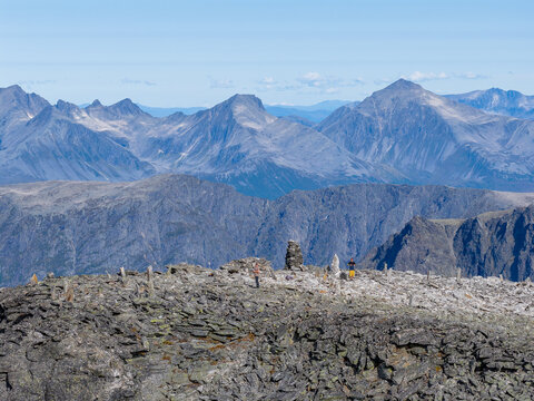 Aerial view of the rocky summit of Kongen mountain with hikers and stone cairns overlooking the vast mountain range in Rauma Municipality, More og Romsdal, Norway.