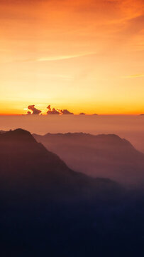 Aerial view of Mount Bromo at sunrise with golden light illuminating the volcanic landscape and clouds in Tosari, East Java, Indonesia.