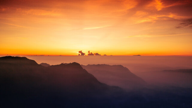Aerial view of Mount Bromo at sunrise with golden light illuminating the misty volcanic landscape and rugged mountain peaks in Tosari, East Java, Indonesia.