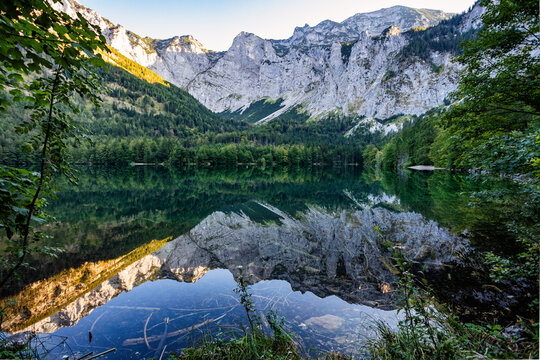 Tranquil alpine lake reflects jagged mountains and lush forest in Austria