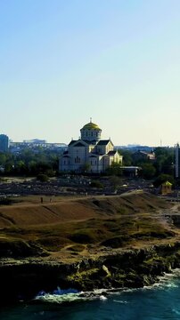 Vertical video. Sevastopol, Crimea. Saint Vladimir Cathedral, gilded dome and white neo-Byzantine walls above ancient stone ruins of Chersonesus Taurica, Drone footage along the Black Sea coast. Dron