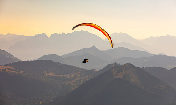 Paraglider flying over majestic Austrian Alps mountains at sunset with hazy layers