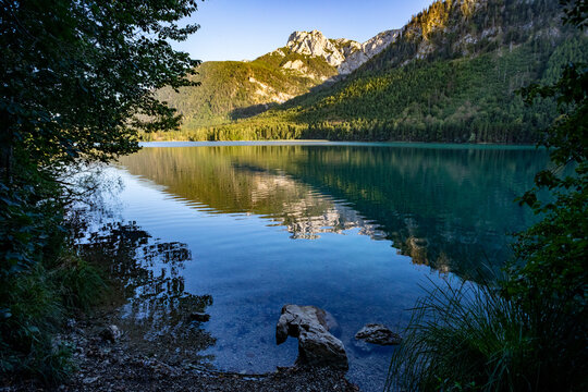 Serene alpine lake Vorderer Langbathsee reflects majestic mountains and lush green forests under a clear blue sky, Austria