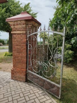 Beautiful ornate iron gate and brick fence column surrounded by green trees
