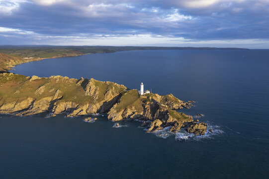 Aerial view of Start Point Lighthouse on a rugged rocky headland surrounded by the sea under a dramatic sky during golden hour in Start Point, England, United Kingdom.