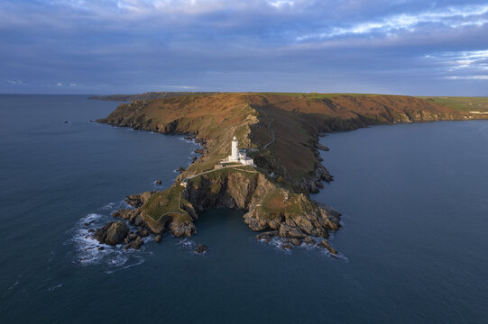 Aerial view of Start Point Lighthouse perched on a rugged rocky headland surrounded by the sea under a dramatic sky in Start Point, England, United Kingdom.