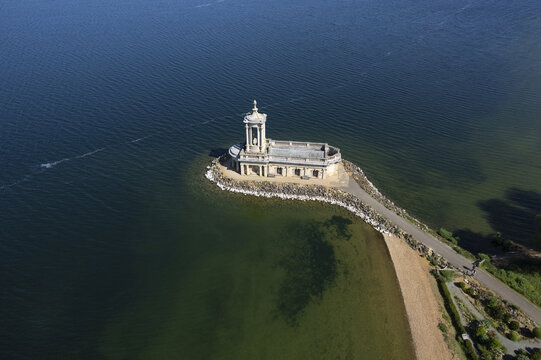 Aerial view of Normanton Church situated on the edge of the reservoir with a stone path leading to the historic building surrounded by the deep blue waters of Rutland Water, Rutland, United Kingdom.
