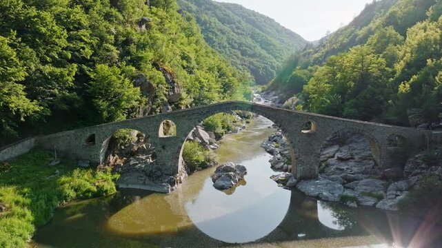 Aerial panorama of medieval Devils Bridge Dyavolski Most over Arda river surrounded by lush green mountains in Bulgaria summer trip vertical slow motion video stock