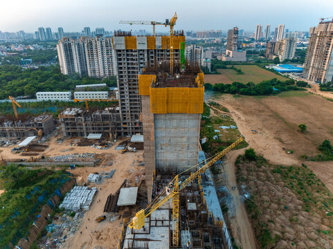Aerial view of a high-rise building under construction with yellow safety netting and tower cranes at a development site in Gurgaon, Haryana, India.
