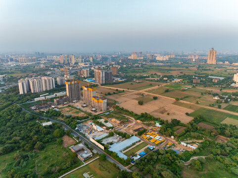 Aerial view of high-rise residential construction sites surrounded by lush greenery and urban development in Gurgaon, Haryana, India.