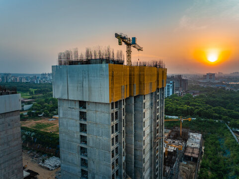Aerial view of a high-rise building under construction with a tower crane on top and yellow safety netting at sunset in Gurgaon, Haryana, India.