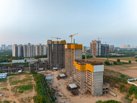 Aerial view of high-rise buildings under construction with cranes and yellow safety netting in a developing urban area in Gurgaon, Haryana, India.
