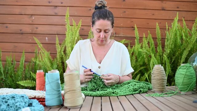 Woman crocheting green yarn with handmade crafts outdoors,  video 4k real time