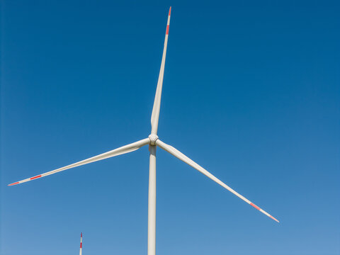Aerial view of a wind turbine with red-tipped blades against a clear blue sky in Buch, Berlin, Berlin, Germany.