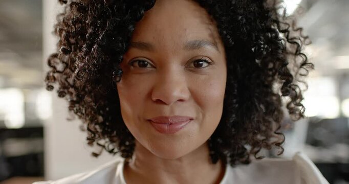 African American woman responding to camera gaze, smiling, laughing in office with blurred monitors