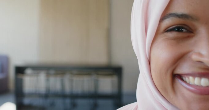 Adult woman in pink headscarf starting smile, leaning, laughing in studio, blurred shelf