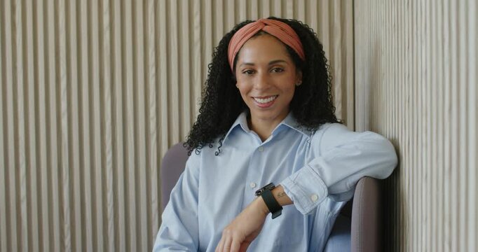 African woman reacting to photographer prompt in lounge corner shifting in armchair smiling more