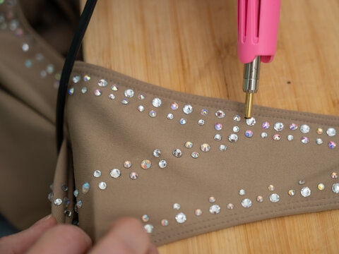 A woman glues rhinestones onto a gymnastics costume using a soldering iron. Hot fix.