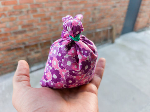 A person holding a small purple floral pattern fabric bag tied with a green rubber band.