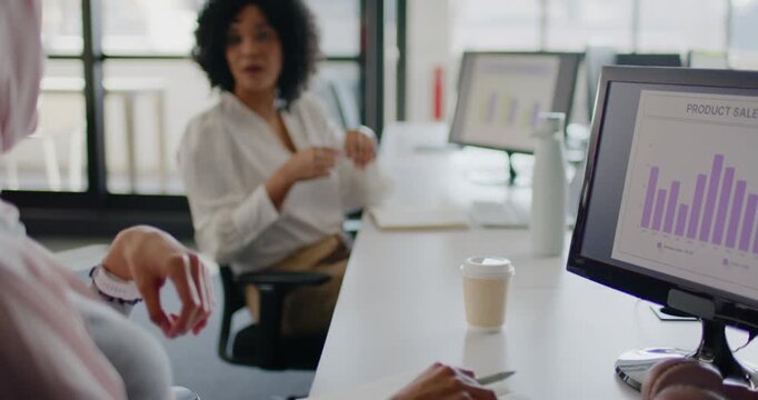 Women coworkers gesturing camera pulling back African-American woman reviewing sales chart at desk