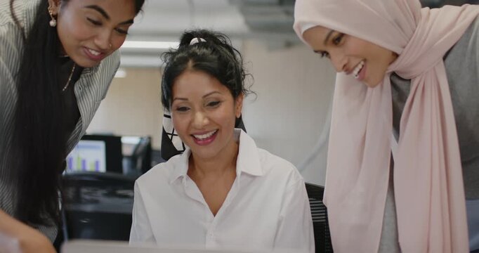 Diverse female team leaning, pointing at laptop at work, reviewing chart after colleague smiling